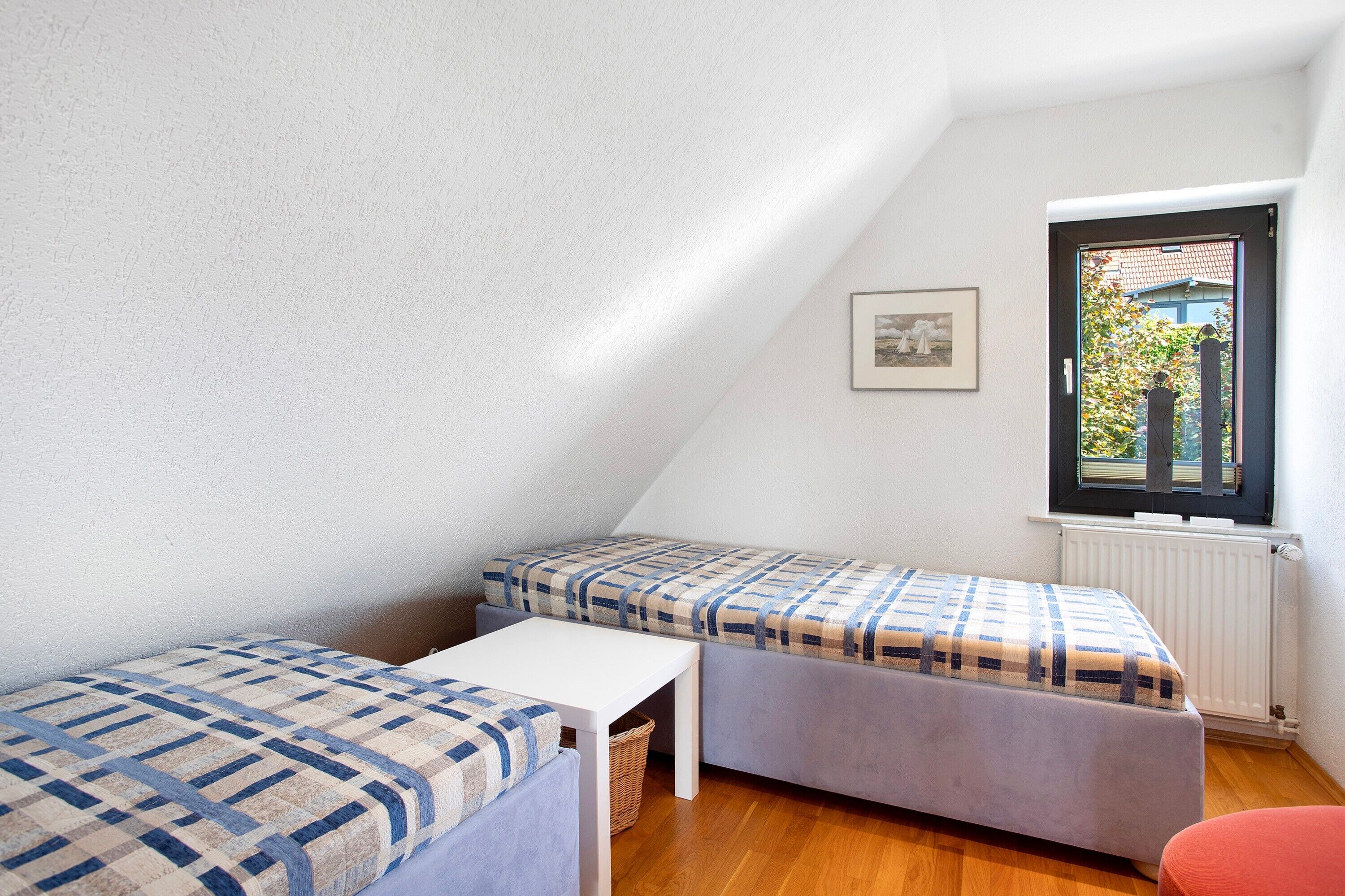 Ein kleiner, dreieckiger Raum mit zwei Betten, einem weißen Tisch und einem Fenster mit Blick auf Grünflächen.