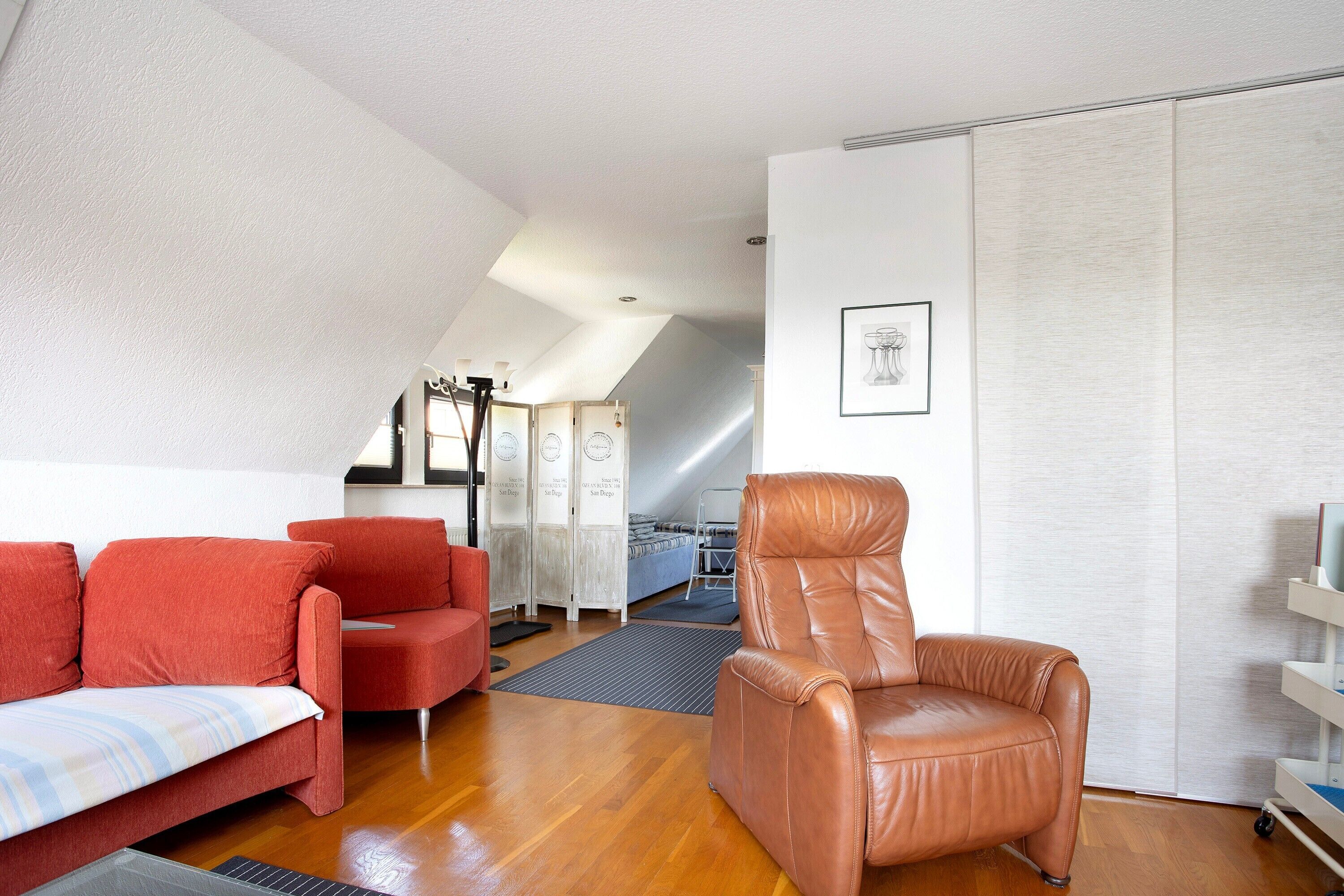 Ein Zimmer mit braunem Ledersessel, roten Sofas, einem Bett und einem weißen Wandschrank.