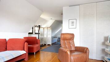 Ein Zimmer mit braunem Ledersessel, roten Sofas, einem Bett und einem weißen Wandschrank.