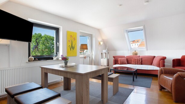 A modern living room with a dining table, benches, a red sofa, and a television.