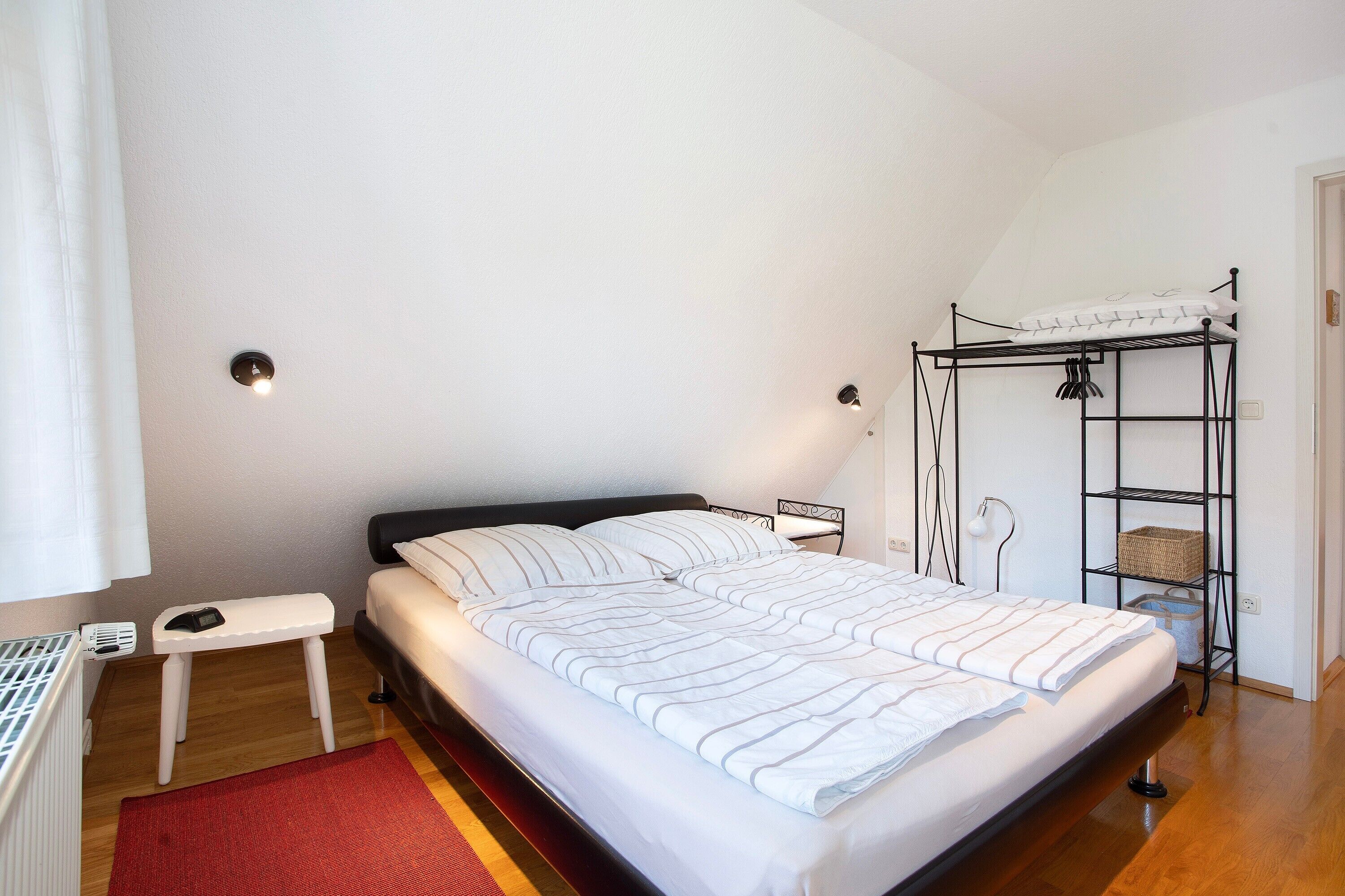 Camera da letto con un letto, comodino, lampada, mensola e un tappeto rosso.