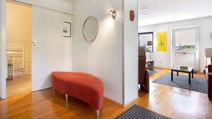 A modern room with a red bench, a round mirror, a small table, and a view of a cityscape through a window.