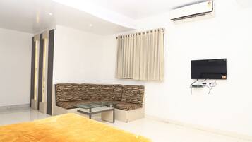 A modern living room with a sofa, a glass coffee table, a flat-screen TV mounted on the wall, and an air conditioning unit.