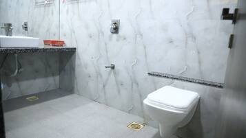 Un baño con pared de mármol blanco, un lavamanos, un inodoro y una zona de ducha.