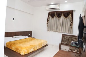 Una habitación de hotel con cama, televisión, banca y unidad de aire acondicionado.