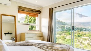 Un dormitorio con una cama grande, un cabecero de madera, una ventana con vistas a un paisaje montañoso y un espejo en la pared.