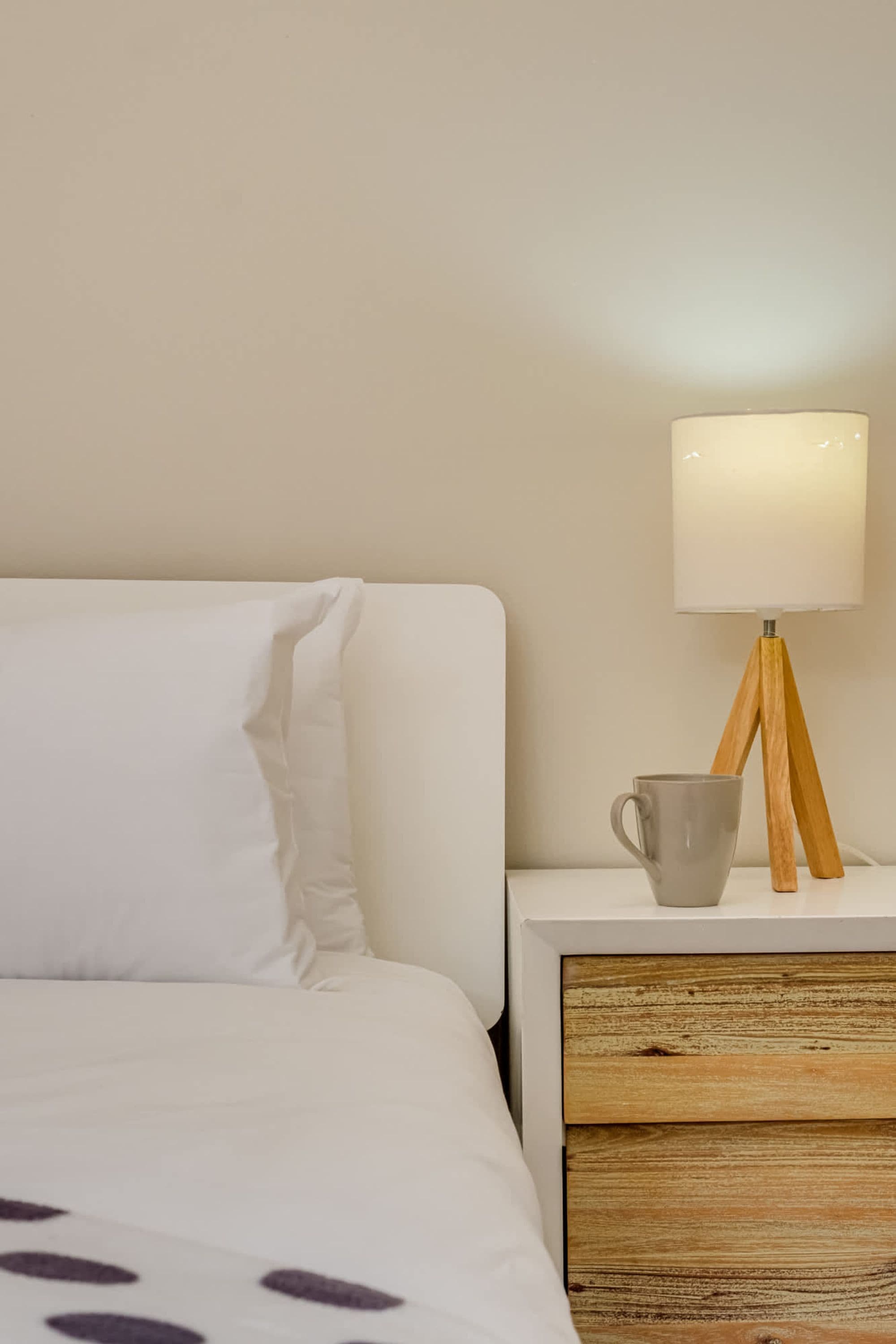 Un lit bien fait, avec une literie blanche, une table de chevet avec une lampe et une tasse.