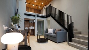 A modern living room with a grey sofa, a coffee table, and a staircase with black railings. - Woodstory Boutique Hotel (Bangkok)