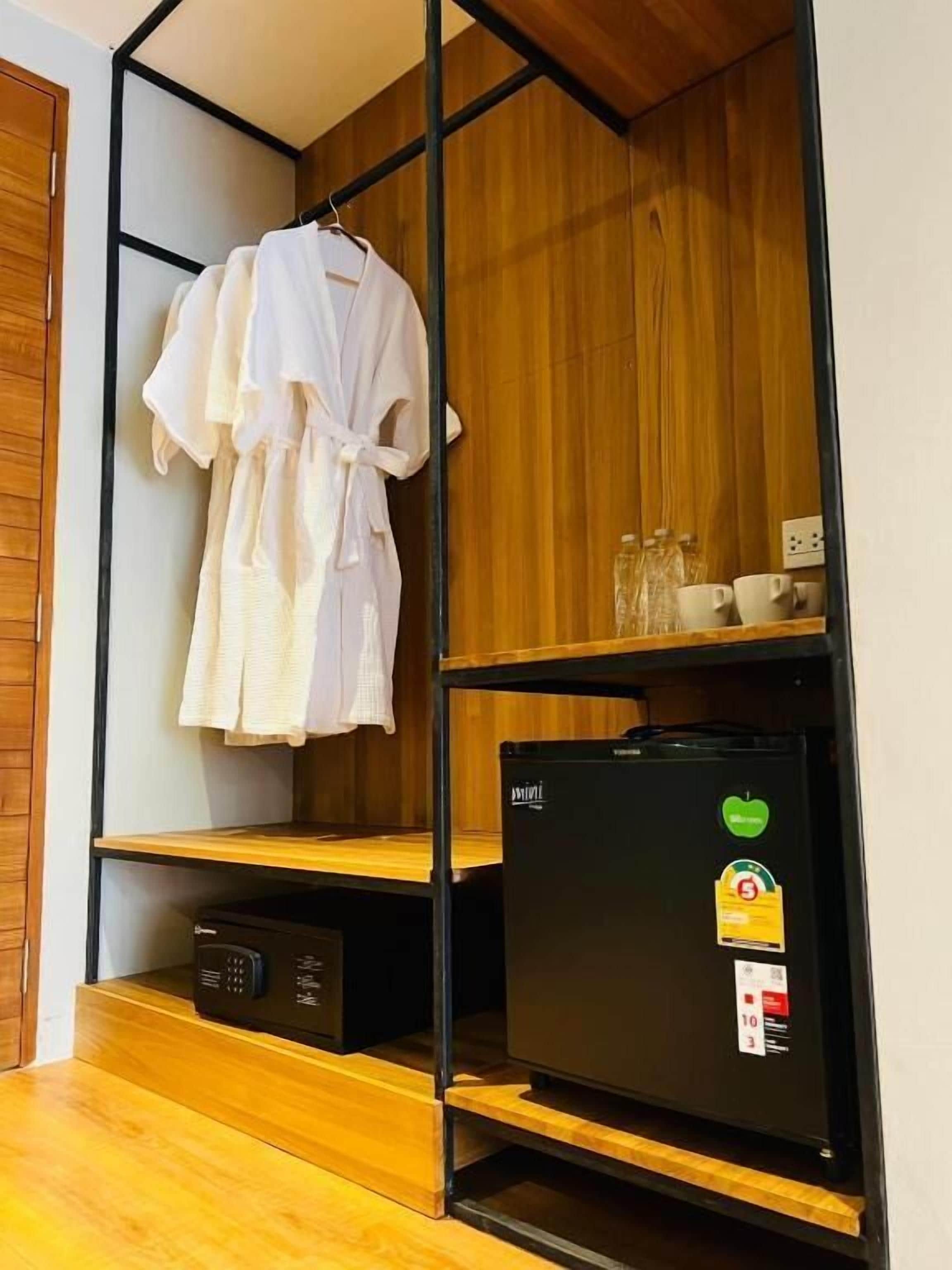 Ein kleines Zimmer mit einem Holzschrank, einem schwarzen Kühlschrank und einem weißen Bademantel, der an dem Schrank hängt.