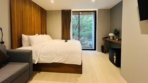 A modern bedroom with a bed, a sofa, a window with curtains, and a small table with a lamp. - Woodstory Boutique Hotel (Bangkok)