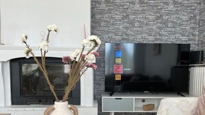 A modern living room with a fireplace, a flat-screen TV, and a white sofa. - La Chaleureuse - Proche Cdg, Parc des Expositions, Disney, Astérix, Paris (Tremblay-en-France)