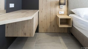 Une chambre à coucher moderne avec un bureau en bois, une table de chevet avec une lampe et un lit recouvert de draps blancs.