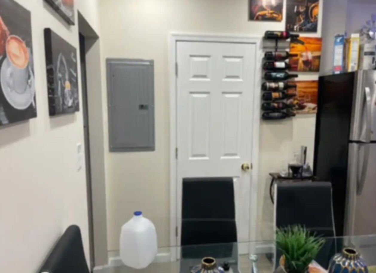 Un comedor con mesa de vidrio, sillas, una puerta blanca y un refrigerador.