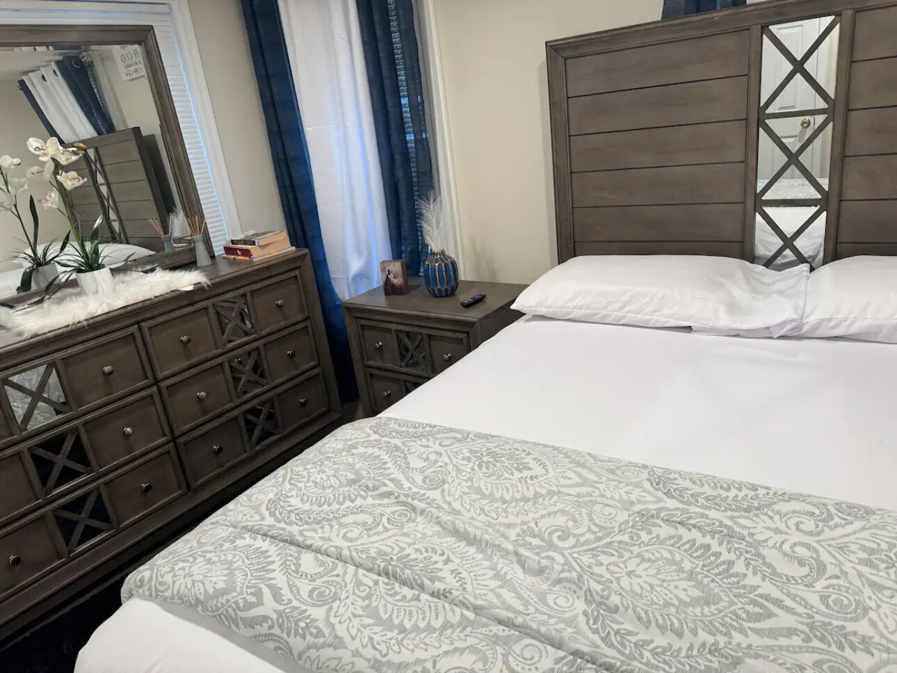 Ein Schlafzimmer mit einem großen Bett, einer Kommode mit Schubladen, einem Spiegel und einer Vase mit Blumen.