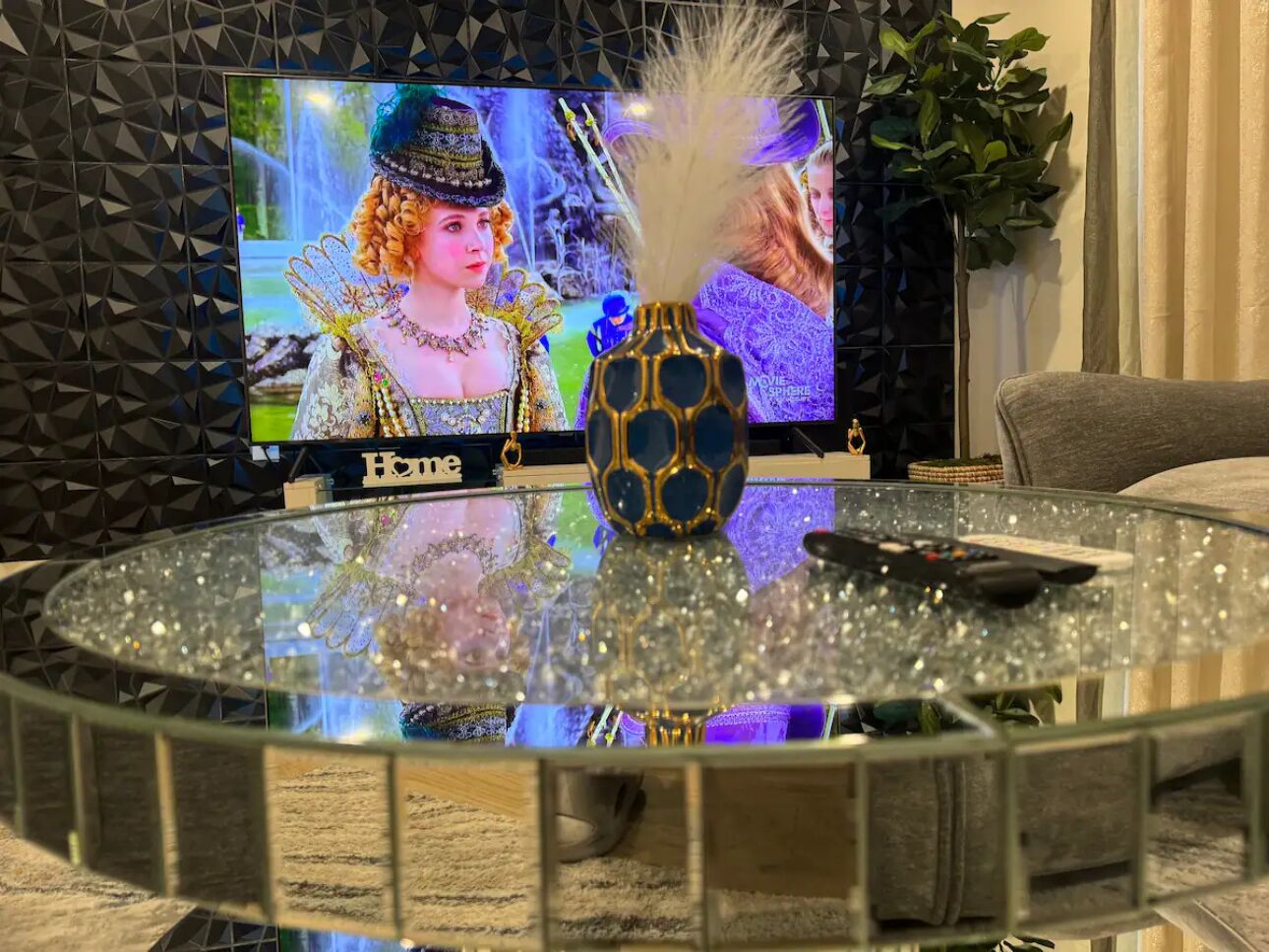 Una mesa de centro redonda de vidrio con un florero decorativo y un control remoto.