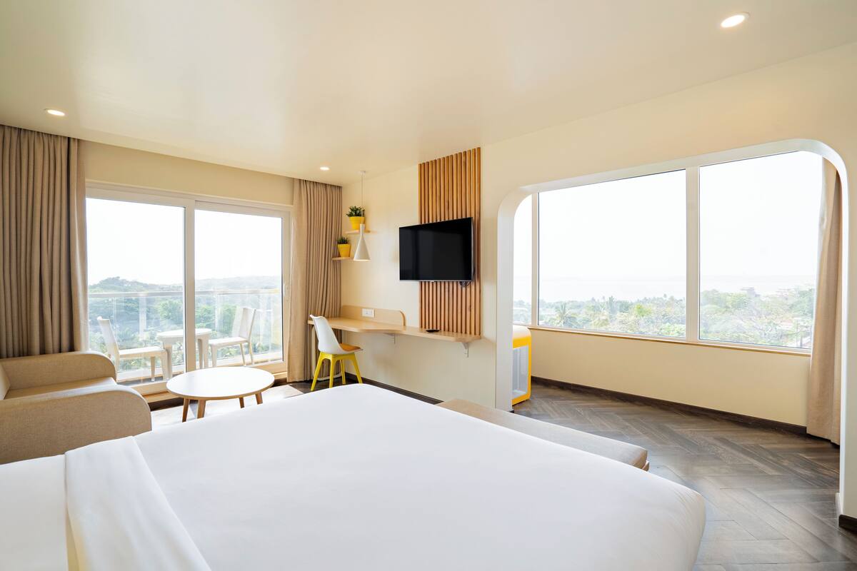 A hotel room with a large bed, a desk, a chair, a small table, and a TV mounted on the wall.