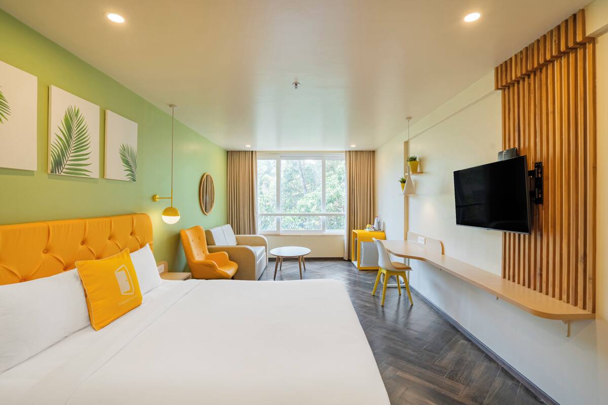 A hotel room with a large bed, a sofa, a small table, and a TV mounted on the wall.