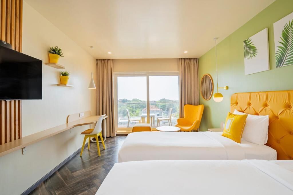 A hotel room with two beds, a desk, a chair, a TV, and a view of the outdoors.