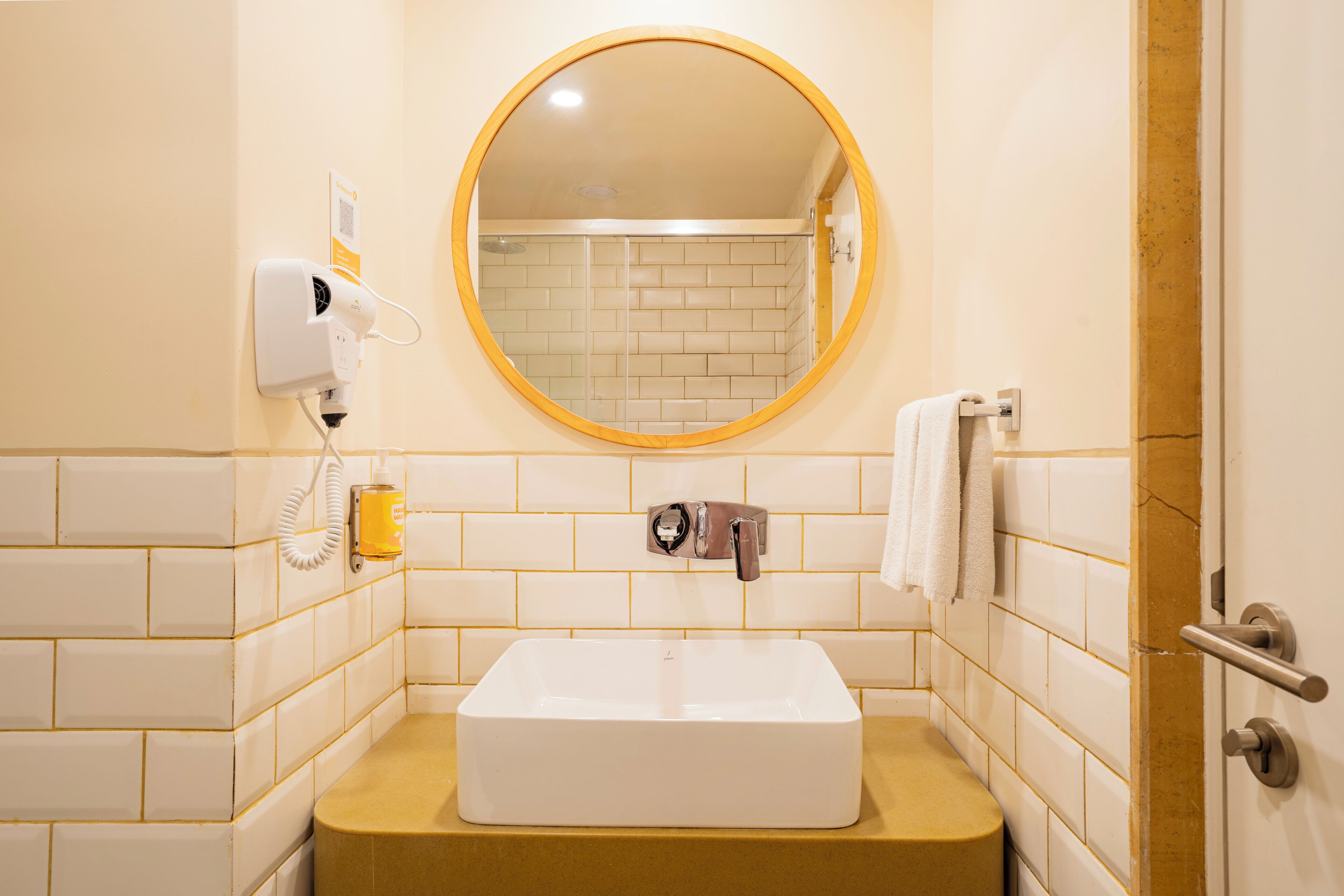 A bathroom with a white sink, a round mirror, a towel rack, and a hand dryer.
