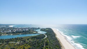 Vue aérienne d’une ville côtière avec une plage, un port de plaisance et une végétation luxuriante.