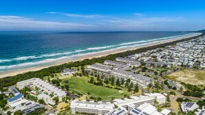 A coastal residential area with a beachfront, a large community center, and multiple apartment buildings. - Luxury Apartment 1206 at Bells Boulevard - Spa suite with park views in a beachfront resort (Kingscliff)