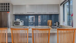 A modern kitchen with a stainless steel refrigerator, a microwave, and a sink. There are wooden chairs and a window with a view of buildings. - Breakwater Views Apartment 2 Cabarita Beach (Cabarita Beach)