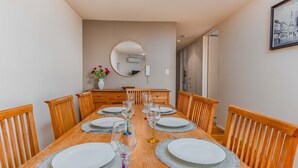 A dining room with a wooden table set for six, a mirror above, and a dresser with a vase of flowers. - Breakwater Views Apartment 2 Cabarita Beach (Cabarita Beach)