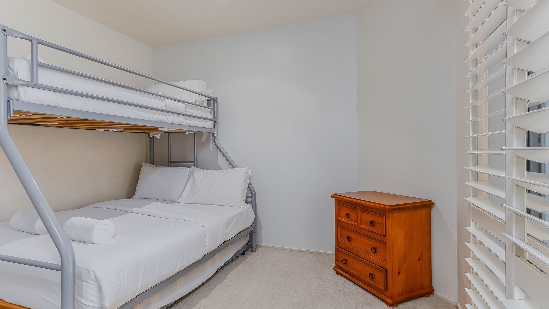 Un lit superposé avec une commode en bois et une étagère blanche.
