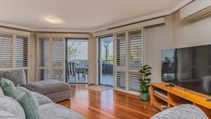 A living room with a TV, sofa, and a balcony with sliding doors. - Breakwater Views Apartment 2 Cabarita Beach (Cabarita Beach)
