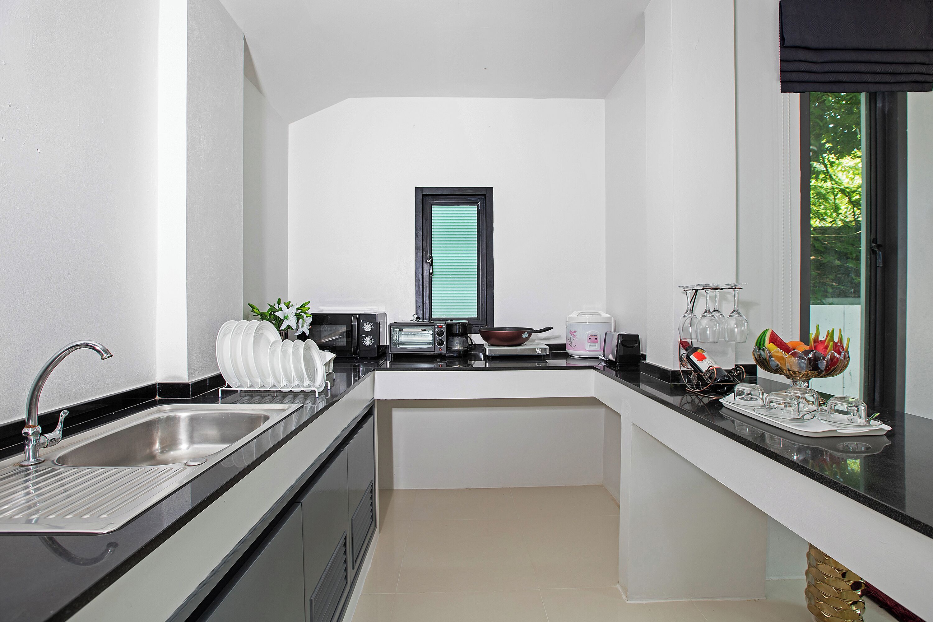 Una cucina moderna con lavello integrato, una finestra con persiane, un fornello e diversi elettrodomestici.