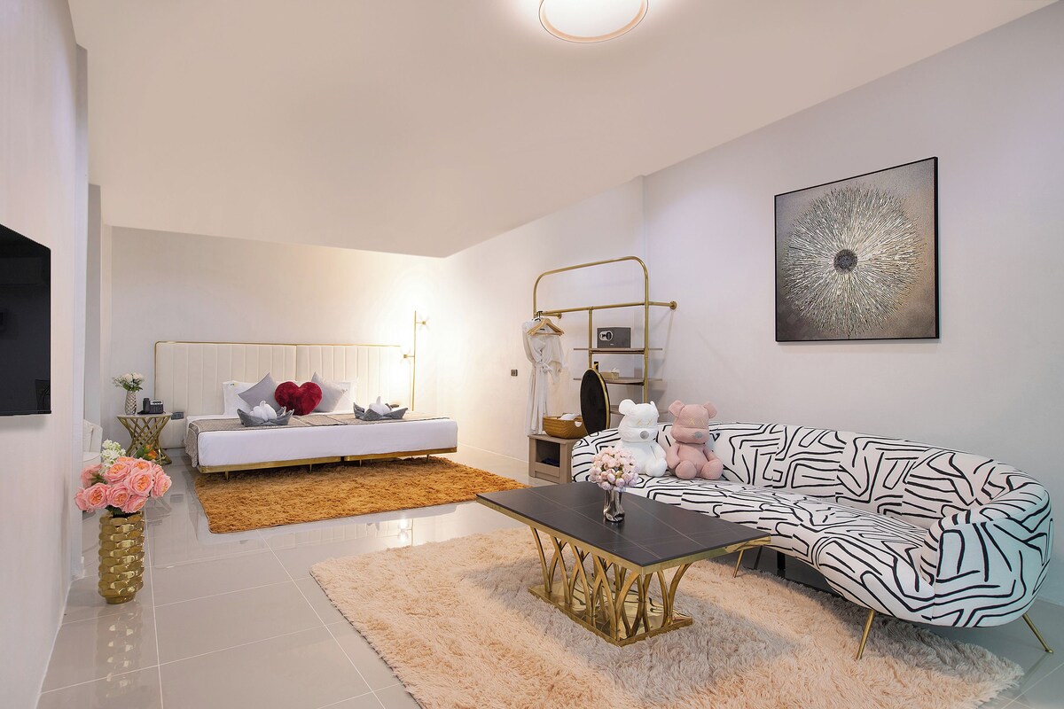 Una sala moderna con sofá, mesa de centro, cama y televisor montado en la pared.
