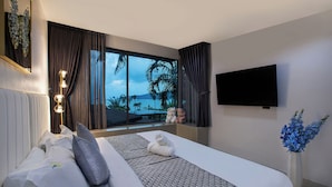 Una moderna camera d'albergo con un letto grande, una TV, vista sull'oceano e una finestra con tende.