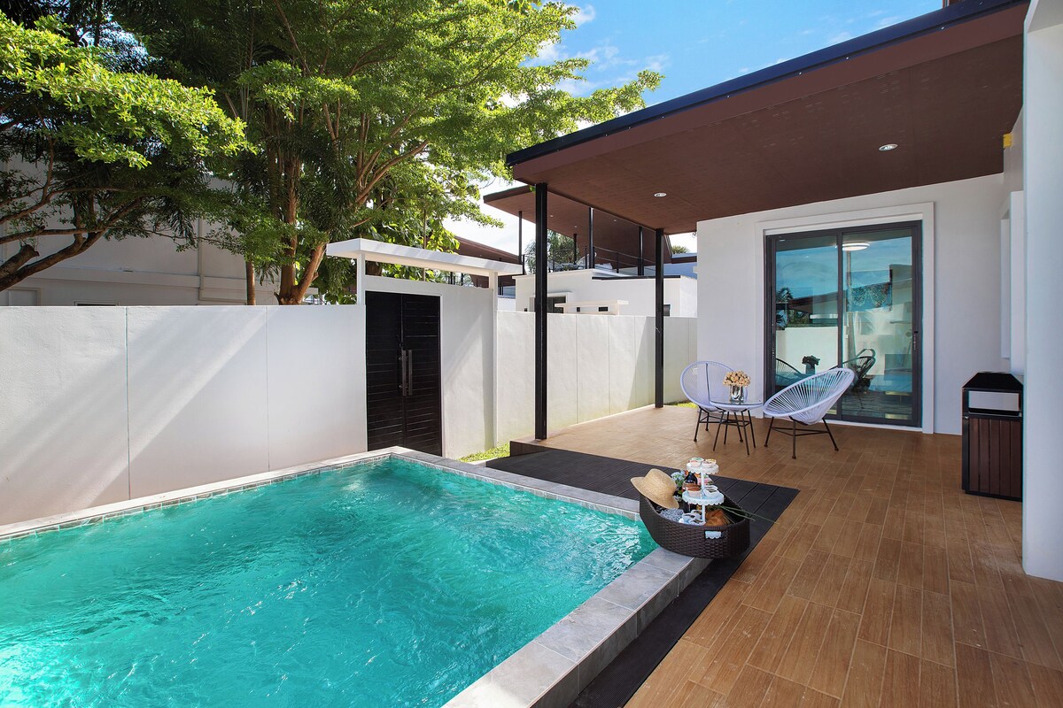 A modern outdoor pool area with a clear pool, a covered seating area, and a glass door leading to a balcony.