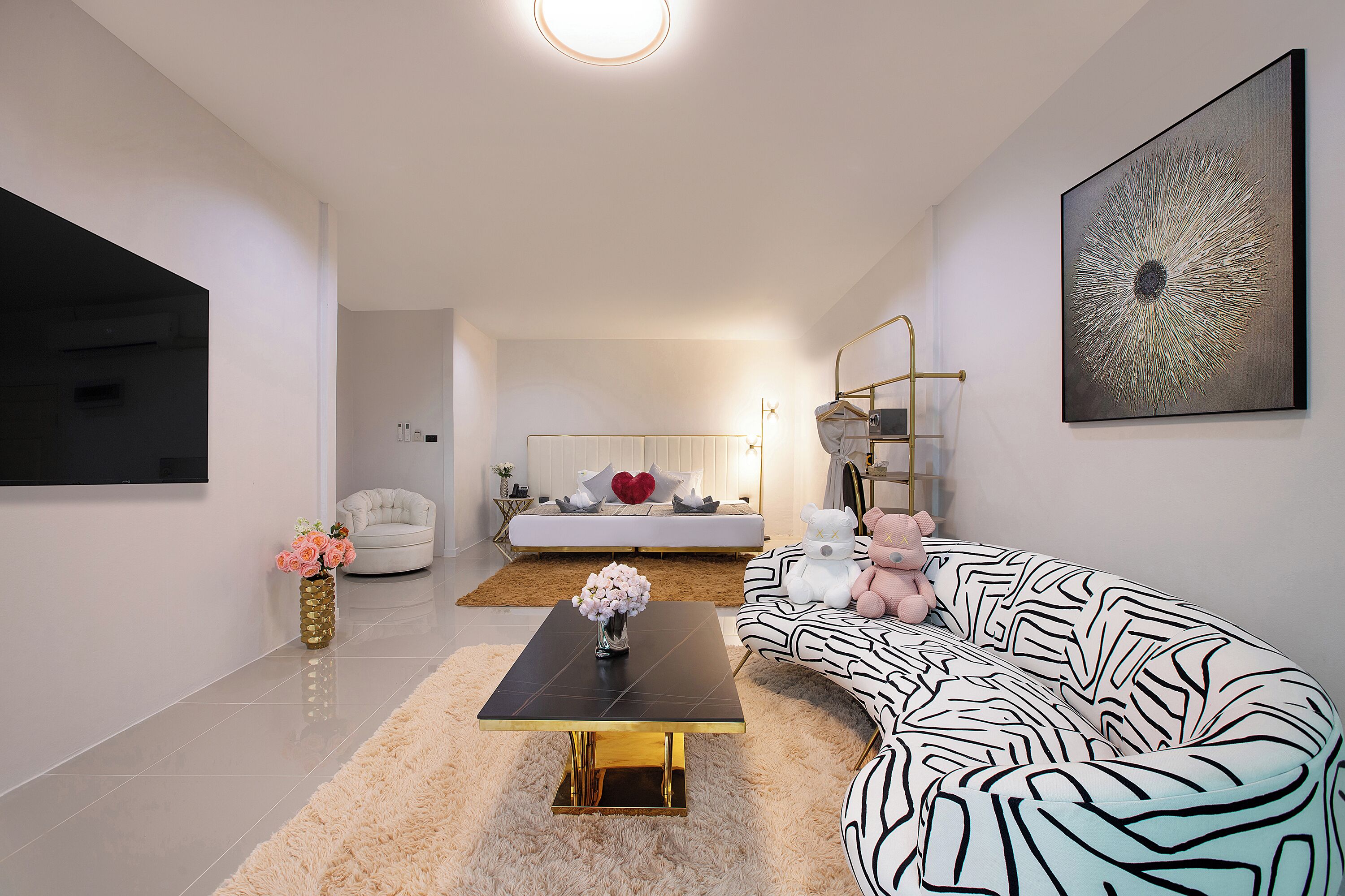 A modern living room with a black coffee table, a white sofa, a patterned sofa, a gold-framed side table, and a large abstract painting on the wall.
