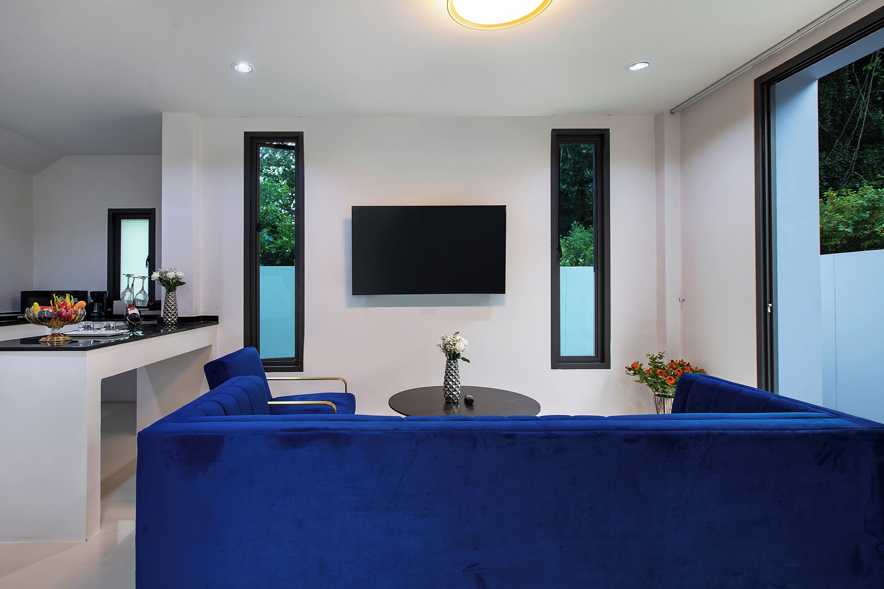 A modern living room with a blue sofa, a small round table, and a flat-screen TV mounted on the wall.