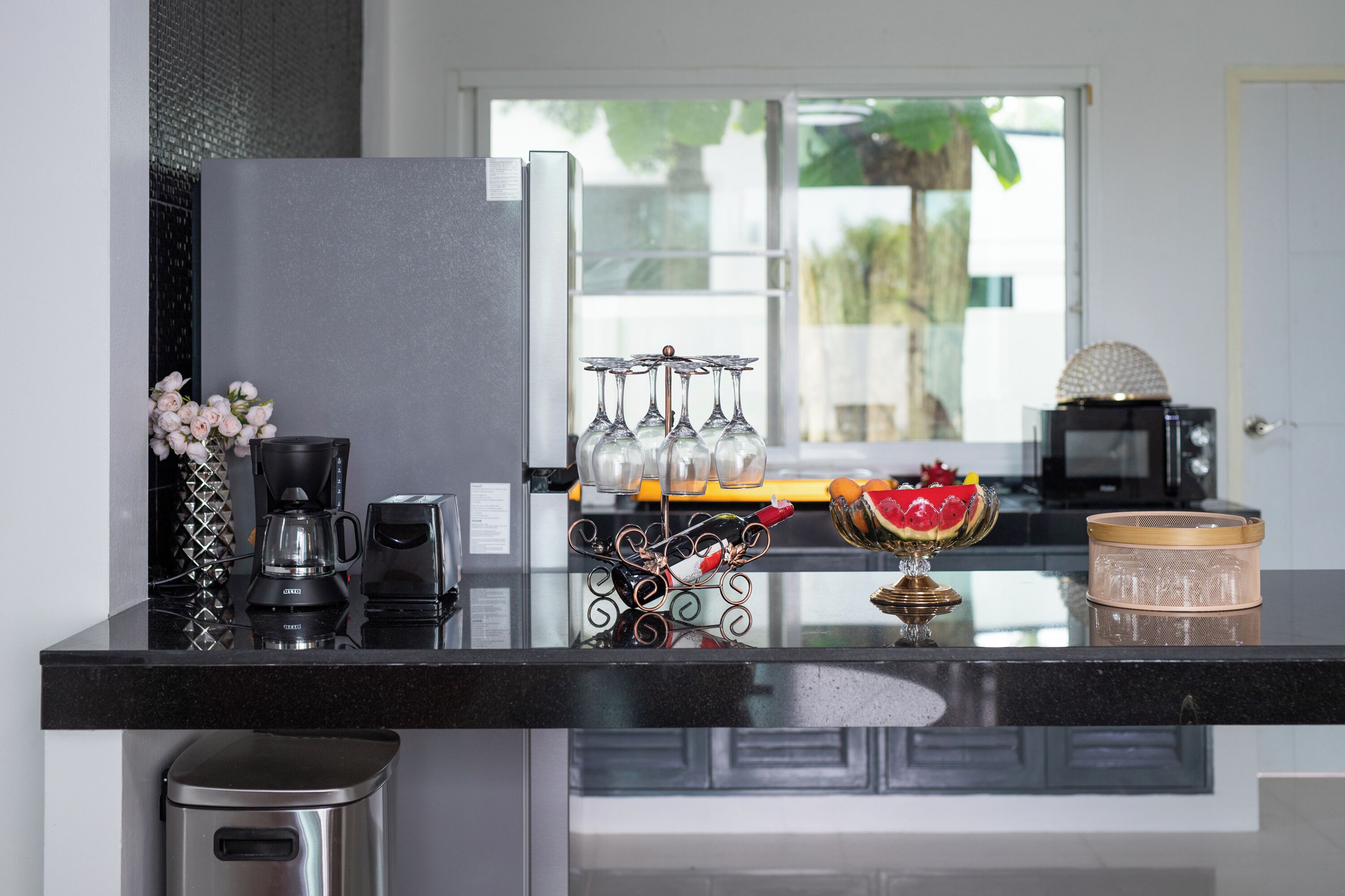 A modern kitchen with a black countertop, stainless steel appliances, and a view of the outdoors through a window.