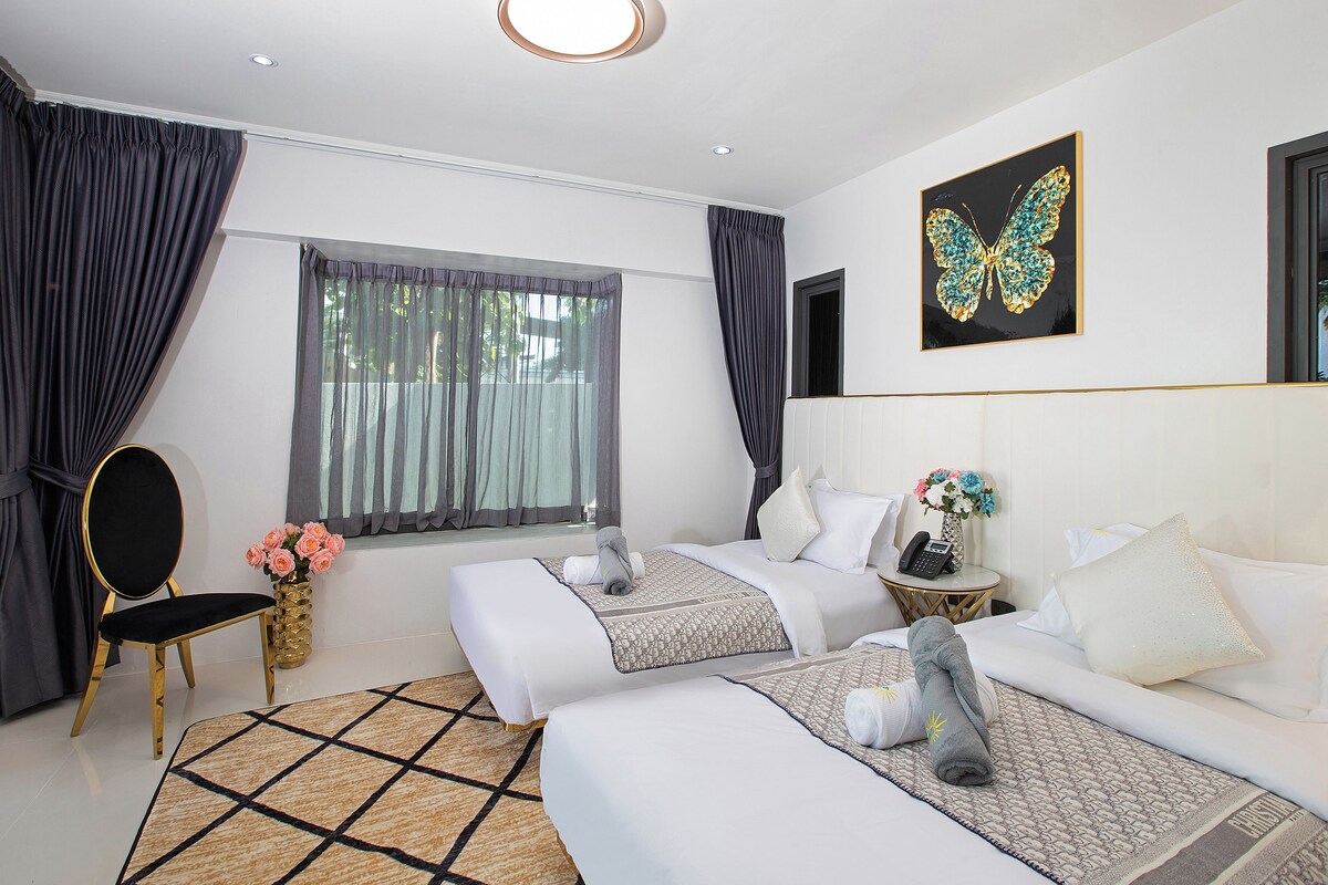 Habitación de hotel con dos camas, una silla, un escritorio, un florero con flores y una obra de arte con temática de mariposas en la pared.
