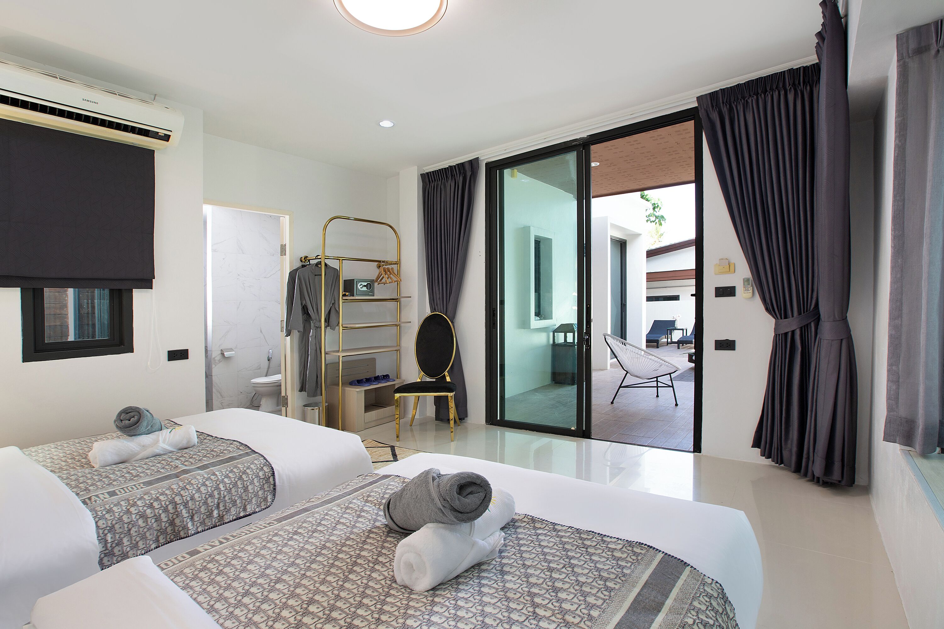 A modern hotel room with two beds, a large sliding glass door to a balcony, a gold-framed chair, and a small seating area with a chair and table.