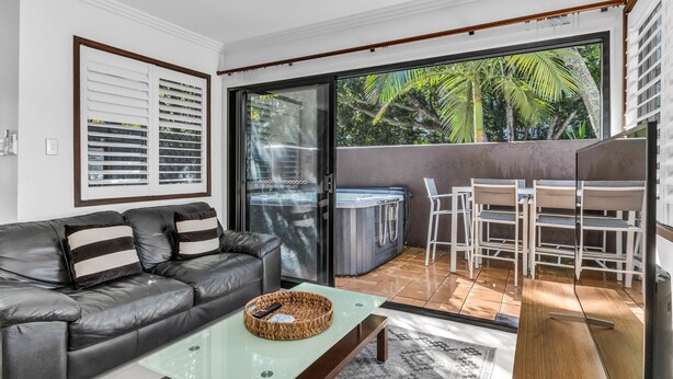 A modern living room with a leather sofa, a glass coffee table, and a hot tub in the background.