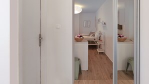 A modern, well-lit room with a wooden floor, a white sofa, a small table with a bowl of fruit, and a green stool. - Cozy Garden Studio (Athens)