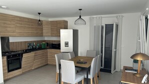 Une cuisine moderne avec des meubles en bois, un four encastré, un four à micro-ondes et un réfrigérateur. On y trouve une table à manger avec des chaises et une lampe.