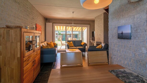 A modern living room with a wooden cabinet, blue sofas, a coffee table, and a large hanging light fixture. - Abbestederweg 24A holiday home in Callanstoog (Callantsoog)