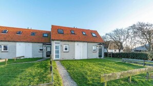A two-story building with a red-tiled roof, a gravel pathway, and a grassy lawn. - Abbestederweg 24A holiday home in Callanstoog (Callantsoog)