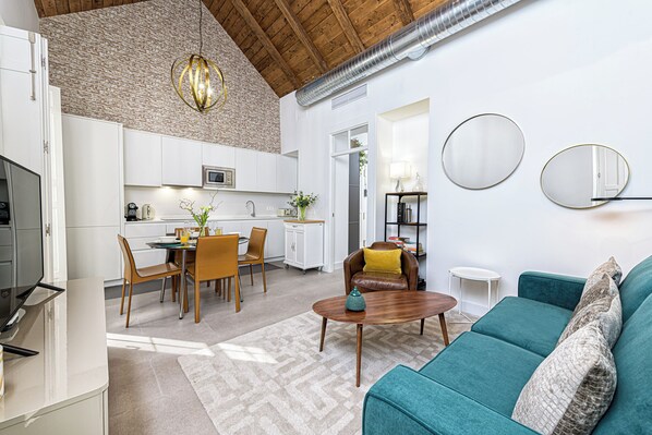 Una cucina moderna con mobili bianchi, un'area pranzo con sedie di legno, un divano color petrolio e un tavolino da caffè.