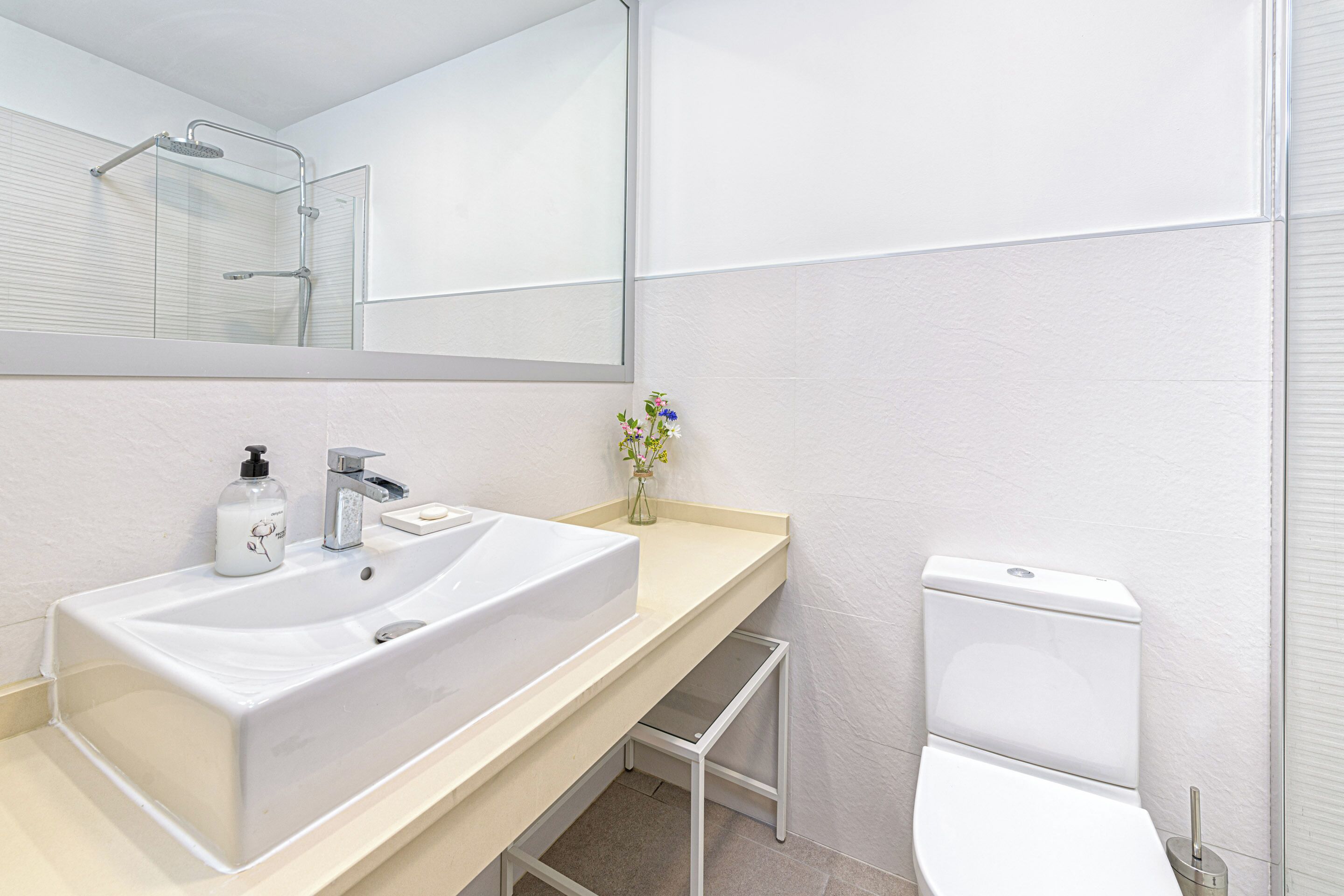 Une salle de bain moderne avec un grand lavabo blanc, un miroir, des toilettes et un petit marchepied pour faciliter l’accès.