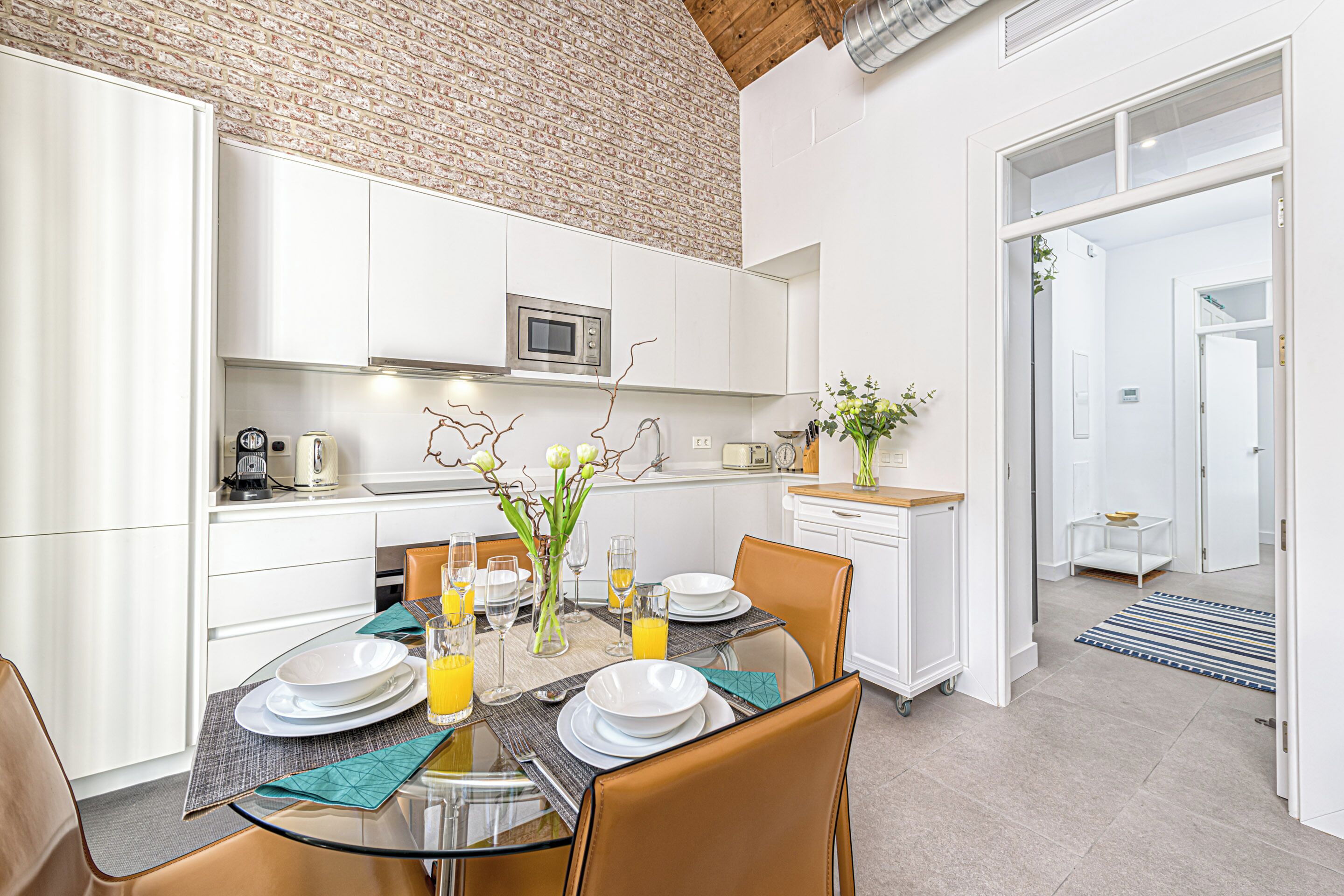 Une cuisine moderne avec des meubles blancs, un four à micro-ondes et un coin repas doté d’une table en verre pour quatre personnes.
