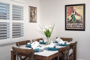 Un coin repas avec une table dressée pour quatre personnes, entourée de chaises en bois. Un vase rempli de fleurs blanches est posé sur la table.