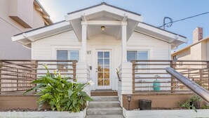 A white two-story house with a front porch, number 87, and a small garden area with potted plants. - Rooftop Retreat - Monterey House - Walk to the Monterey Aquarium (Monterey)