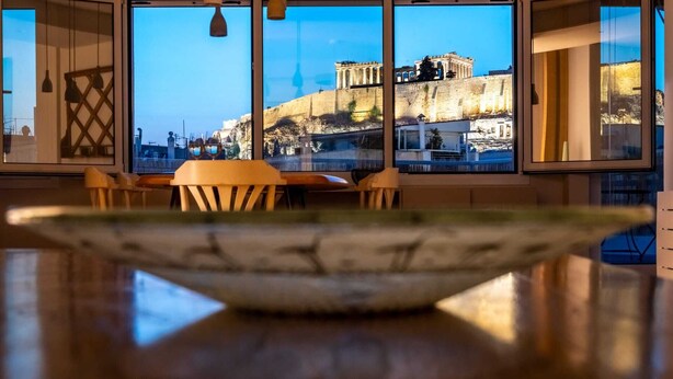 A dining area with a view of ancient ruins through large windows. - Unique 2BR Penthouse with Stunning Acropolis View (Athens)