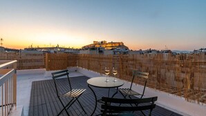 A rooftop terrace with a table and chairs, two glasses of wine, and a view of a historic building at sunset. - Unique 2BR Penthouse with Stunning Acropolis View (Athens)